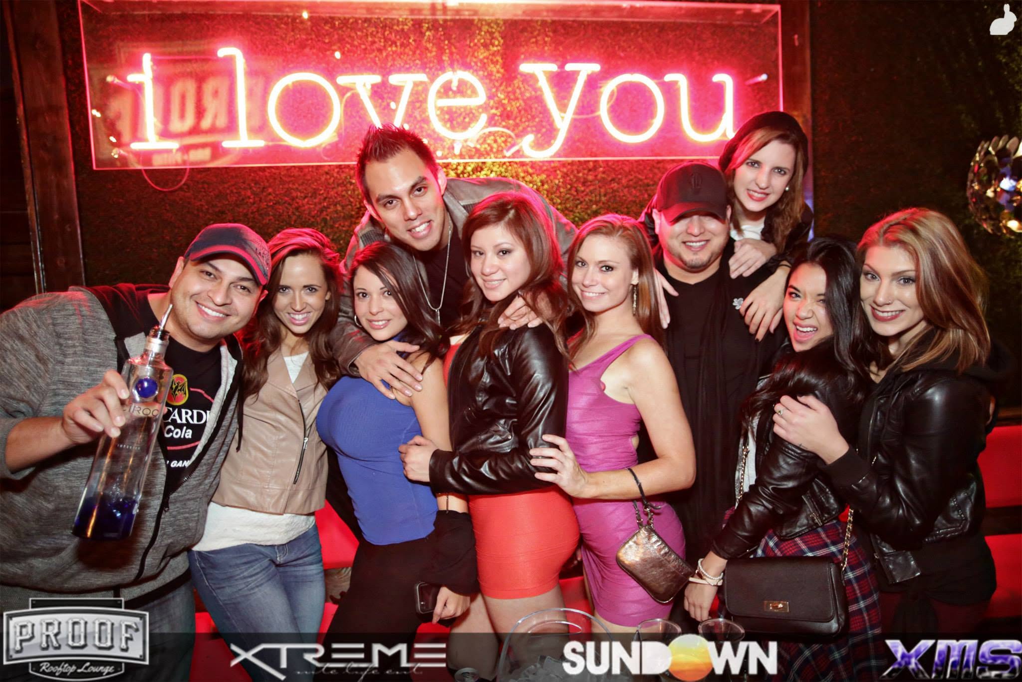 Cixx surrounded by friends beneath the neon at a Midtown nightlife event